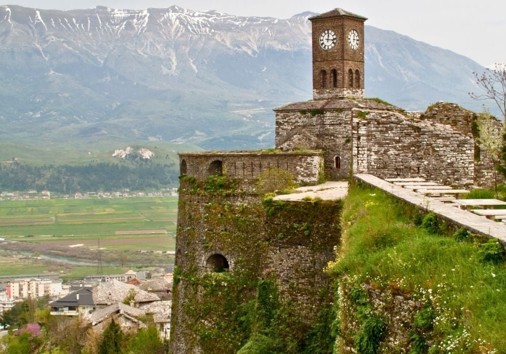 View of Gjirokaster Castle with its prominent tower, situated on a lush green hillside.