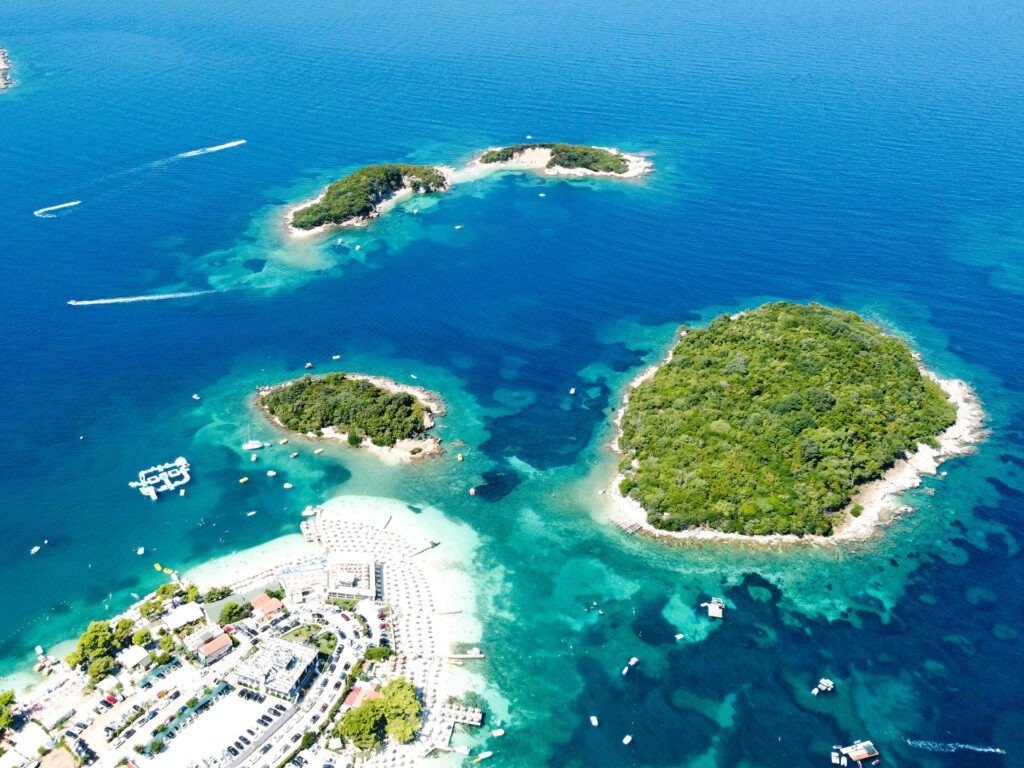 Aerial view of Ksamil Island with azure waters, sandy shore, and vibrant greenery.