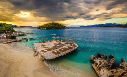 Sunset view of Ksamil Island with golden light illuminating azure waters and sandy shore.