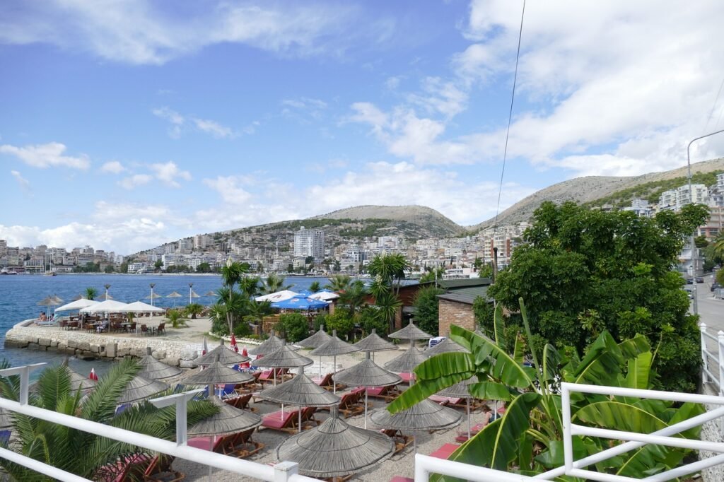 View of Saranda's coast from a balcony overlooking azure waters and cafes along the promenade.