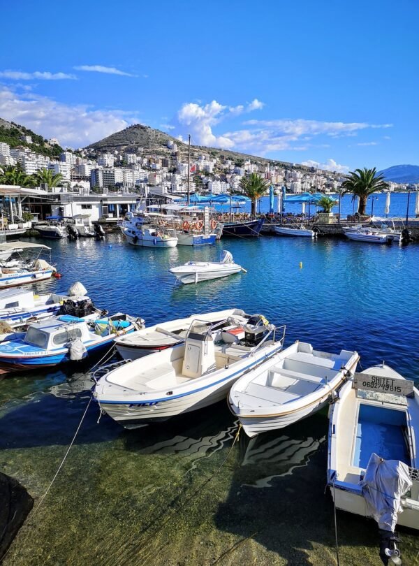 Seascape of Saranda's coast with small boats near the promenade against a backdrop of blue skies and azure waters.