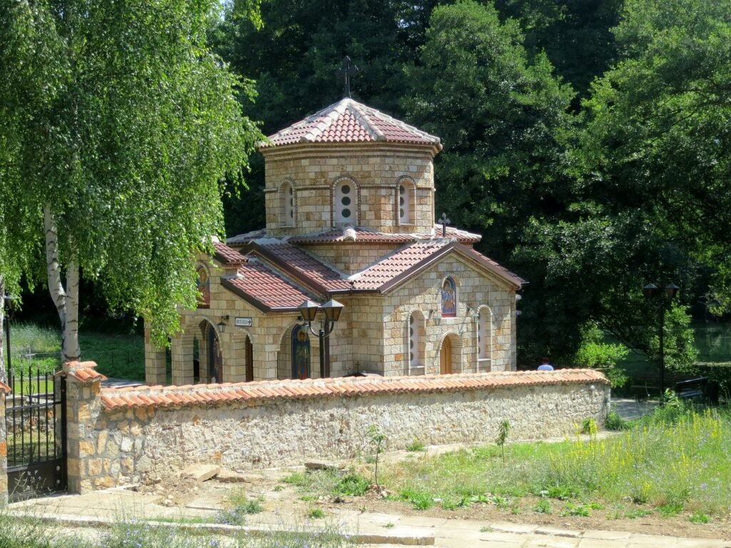 View of the small stone church at the Monastery of Voskopoja, set in a gray, tree-filled landscape.